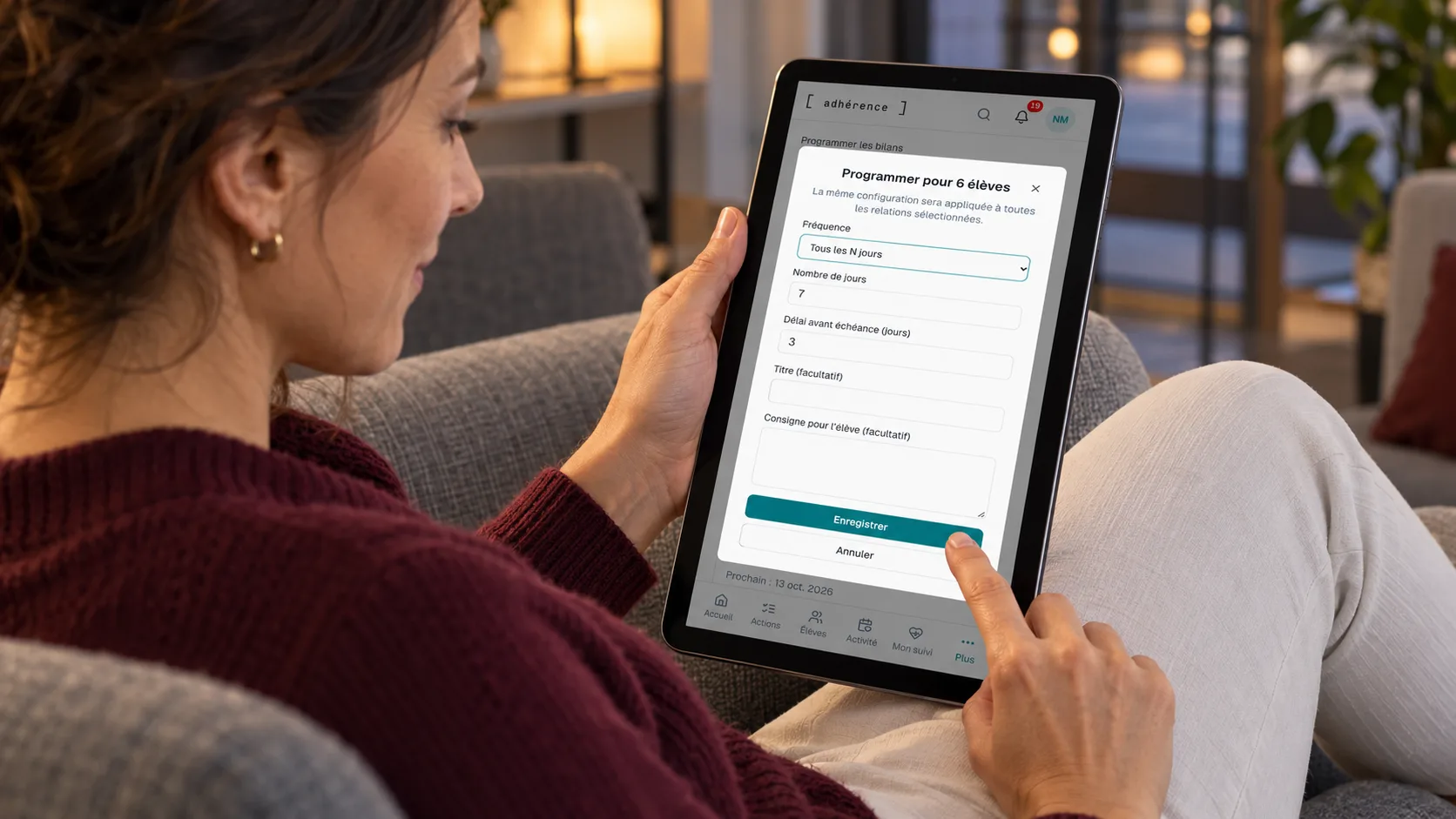 Trainer configuring recurring Adhérence check-ins on a tablet while seated in a coworking lounge armchair.