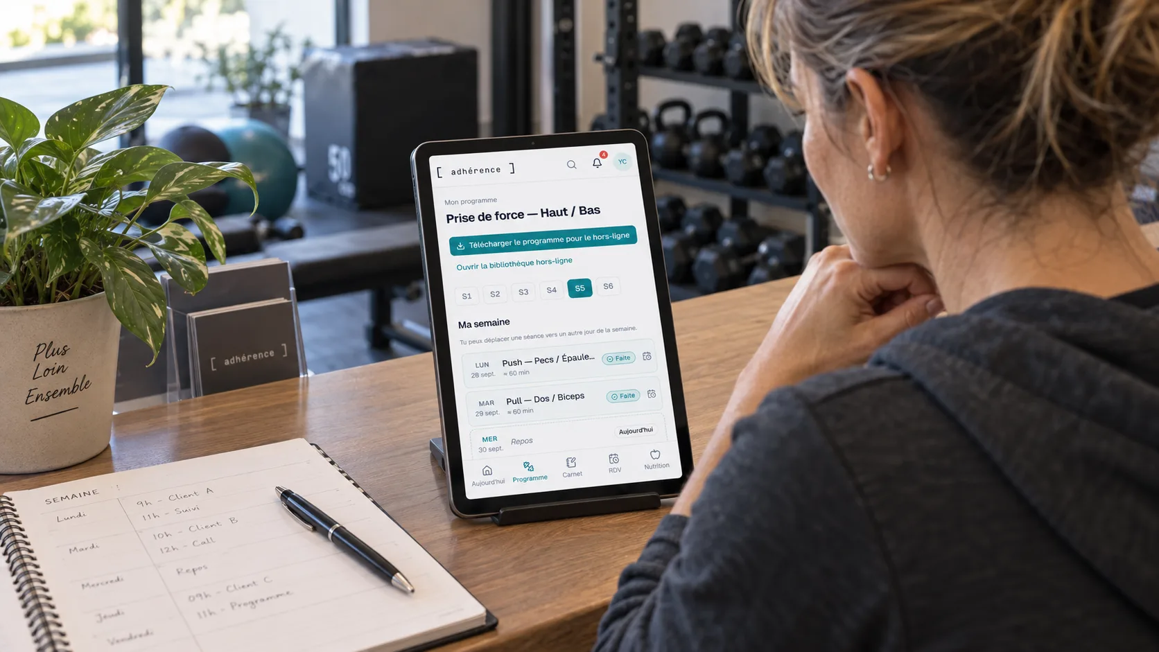 Personal trainer preparing her week with an Adhérence programme on a tablet and a paper diary.