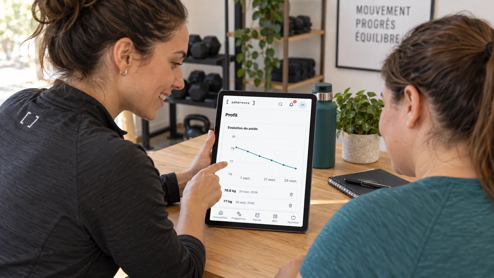 Coach et cliente discutant de l’historique de poids Adhérence affiché sur une tablette.