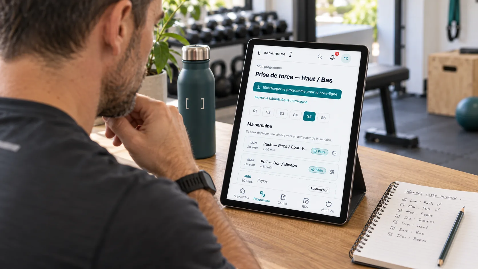 Personal trainer reviewing an Adhérence training programme on a tablet beside planning notes.