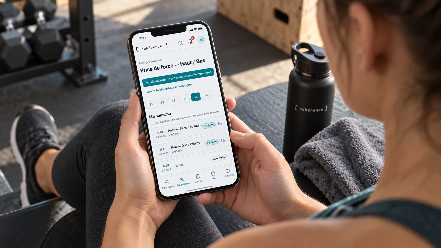 Élève retrouvant son programme Adhérence sur téléphone pendant un temps de repos en salle de musculation.